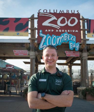 A security team member is standing in front of the Columbus Zoo and Aquarium sign at the front gate